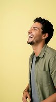 Young man with dark curly hair and facial hair, appearing to be of Middle Eastern or Mediterranean descent, wearing olive button-up shirt over gray t-shirt, smiling broadly in profile against yellow background for lifestyle and portrait use.