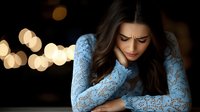 Young woman in blue lace dress showing emotional distress against blurred bokeh lights background, expressing sadness, anxiety and depression in dramatic lighting.