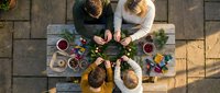 Family enjoying outdoor picnic meal together on wooden table viewed from above with fresh food and drinks on sunny day.
