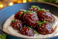 Glazed meatballs served on creamy mashed potatoes, garnished with fresh chopped herbs and sesame seeds, close-up view in dark plate with bokeh lights.