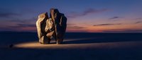 Mysterious ancient stone sculpture glowing with warm light against dramatic twilight sky in desert landscape for fantasy and adventure concepts.