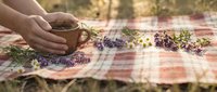 Hands arranging dried lavender flowers and herbs on rustic wooden table in warm sunlight for natural aromatherapy and wellness preparation.