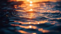 Mesmerizing ocean waves ripple at sunset creating golden reflections on dark blue water surface, with bokeh light effects and gentle motion blur patterns.