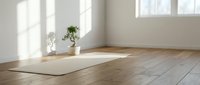 Empty yoga studio with mat on wooden floor and natural sunlight streaming through windows for meditation and wellness practice.
