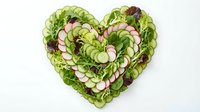 Fresh green salad with radish slices arranged in heart shape on white background, promoting healthy eating and vegetarian nutrition for wellness campaigns.