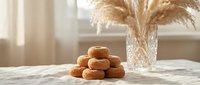 Stack of golden brown donuts arranged on marble surface with dried pampas grass in crystal vase creating warm minimalist kitchen scene for bakery marketing.
