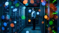 Male IT technician working in modern server room with colorful digital network overlay effects representing data connectivity and cloud computing technology.