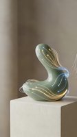 Contemporary glass sculpture with organic curved form in translucent green and gold tones, displayed on white pedestal. Suitable for modern art, interior design, and luxury home decor projects.