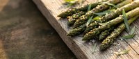 Fresh green asparagus spears arranged on rustic wooden cutting board with herbs, ready for healthy cooking and gourmet meal preparation.
