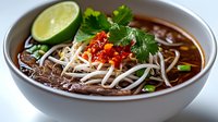 Vietnamese pho soup with beef, rice noodles, fresh herbs and lime in white bowl. Traditional Asian comfort food with cilantro garnish and chili flakes.