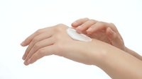 Caucasian woman applying white moisturizing cream or lotion to her hand for skincare, cosmetics, beauty, and wellness product promotion.