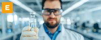 Laboratory scientist in protective gloves holding glass vial with clear liquid against blurred research facility background. Modern medical research concept.