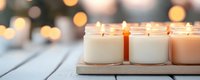 Glowing aromatic candles in glass jars on wooden tray create cozy atmosphere with soft bokeh lights in background, perfect for spa and relaxation settings.