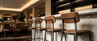 Modern bar stools with wooden backs and metal frames positioned at a marble counter in an upscale restaurant or lounge interior with warm lighting.