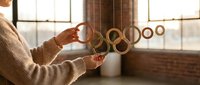 Woman in cozy sweater holding handmade wooden ring mobile in sunlit loft studio, warm tones, artisan home decor and interior design concept.