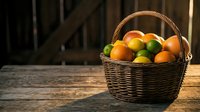 Fresh citrus fruits in wicker basket on rustic wooden table with warm sunlight, featuring oranges, lemons and limes for healthy eating and cooking.
