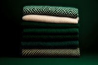 Stack of folded knitted sweaters in green and beige tones on dark background, cozy autumn winter fashion concept.