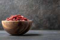 Dried goji berries in wooden bowl on dark surface with textured background for healthy eating and superfood nutrition concepts.