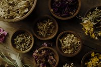 Dried medicinal herbs and flowers in wooden bowls on dark background, top view. Natural healing ingredients for alternative medicine and herbal tea preparation.