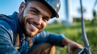 Happy young bearded construction worker in hard hat smiling at camera on building site. Professional contractor portrait for safety and teamwork concepts.