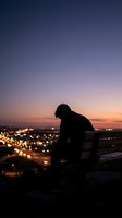 Silhouette of contemplative man sitting alone at sunset overlooking city lights, expressing solitude, reflection and urban evening atmosphere.