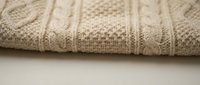 Cozy beige cable knit sweater fabric with intricate braided patterns and textured stitching for fashion and textile design projects.