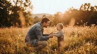 Young Caucasian father bonding with toddler in golden sunlit meadow, sharing a tender moment of love and family connection outdoors.