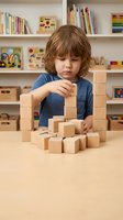 Young boy with curly brown hair building tower with wooden blocks in playroom with colorful books and educational toys on shelves behind him.