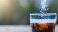 Refreshing dark soda drink in glass with fizzy bubbles rising and condensation drops on surface against blurred background, close up macro photography.