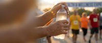 Runner holding water bottle during marathon race with participants in background at sunset for hydration and endurance sports events.