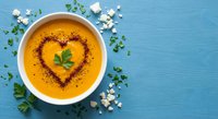 Creamy pumpkin soup with heart-shaped spice garnish and fresh herbs on blue wooden background for healthy comfort food recipes and autumn cooking.