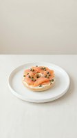 Bagel topped with smoked salmon, cream cheese, and capers on white plate against neutral background, suitable for food styling and culinary content.