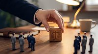 Professional hand placing wooden block with justice scales symbol among business figurines on office desk representing legal decision-making and corporate governance.