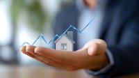 Professional in business attire holds digital house icon with ascending graph line, representing growth in real estate market and property investment trends.