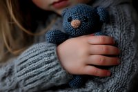 Child holding handmade knitted teddy bear toy in cozy gray sweater. Soft comfort object for emotional support and childhood development activities.