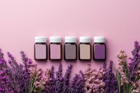 Small glass jars with white lids arranged in row on pink background with fresh lavender flowers border, aromatherapy and natural cosmetics concept.