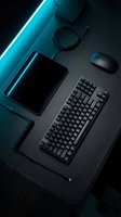 Modern gaming workspace setup with mechanical keyboard, wireless mouse, tablet and cables on dark surface with cyan neon lighting for tech and productivity content.