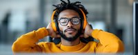 Young African American man wearing yellow sweater and headphones smiling while listening to music. Modern lifestyle portrait with glasses and dreadlocks in panoramic format.