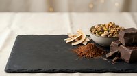 Dark chocolate pieces with cocoa powder and nuts on slate board for gourmet dessert recipes and culinary presentations.