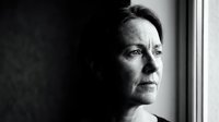 Thoughtful middle-aged woman gazing through window in contemplative black and white portrait showing introspection and emotional depth.
