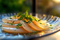 Fresh scallop sashimi garnished with microgreens and herbs on blue-rimmed ceramic plate, soft natural lighting creates appetizing highlights on seafood delicacy.
