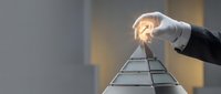 Man in business attire placing glowing lightbulb on top of pyramid structure, symbolizing innovation, leadership and success in corporate strategy and goal achievement.