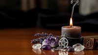 Mystical altar setup with burning candle, amethyst crystals, pentagram pendant and ritual elements for spiritual practices and meditation ceremonies.