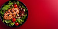 Grilled chicken breast with quinoa salad, cherry tomatoes and fresh arugula leaves on black plate against red background with copy space.