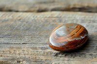 Polished agate stone with natural brown and white striped pattern on rustic wooden surface, showcasing mineral's smooth texture and organic swirling layers.