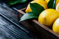 Fresh yellow lemons with green leaves in rustic wooden box on dark wooden background. Close up view with selective focus for food photography and design.
