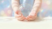 Hands gently holding transparent crystal ball with rainbow light reflections creating magical atmosphere for fortune telling and spiritual guidance.
