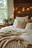 Cozy bedroom interior with knitted bedding, string lights on wooden wall, and natural window light creating warm rustic atmosphere for home decor.