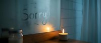 Candlelight glowing near a foggy window with the word Sorry written on it, evoking emotions of regret, apology, and reconciliation.