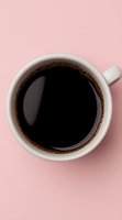 White ceramic cup filled with black coffee on pink background, viewed from above. Fresh brewed coffee shows subtle foam around edges creating minimalist composition.